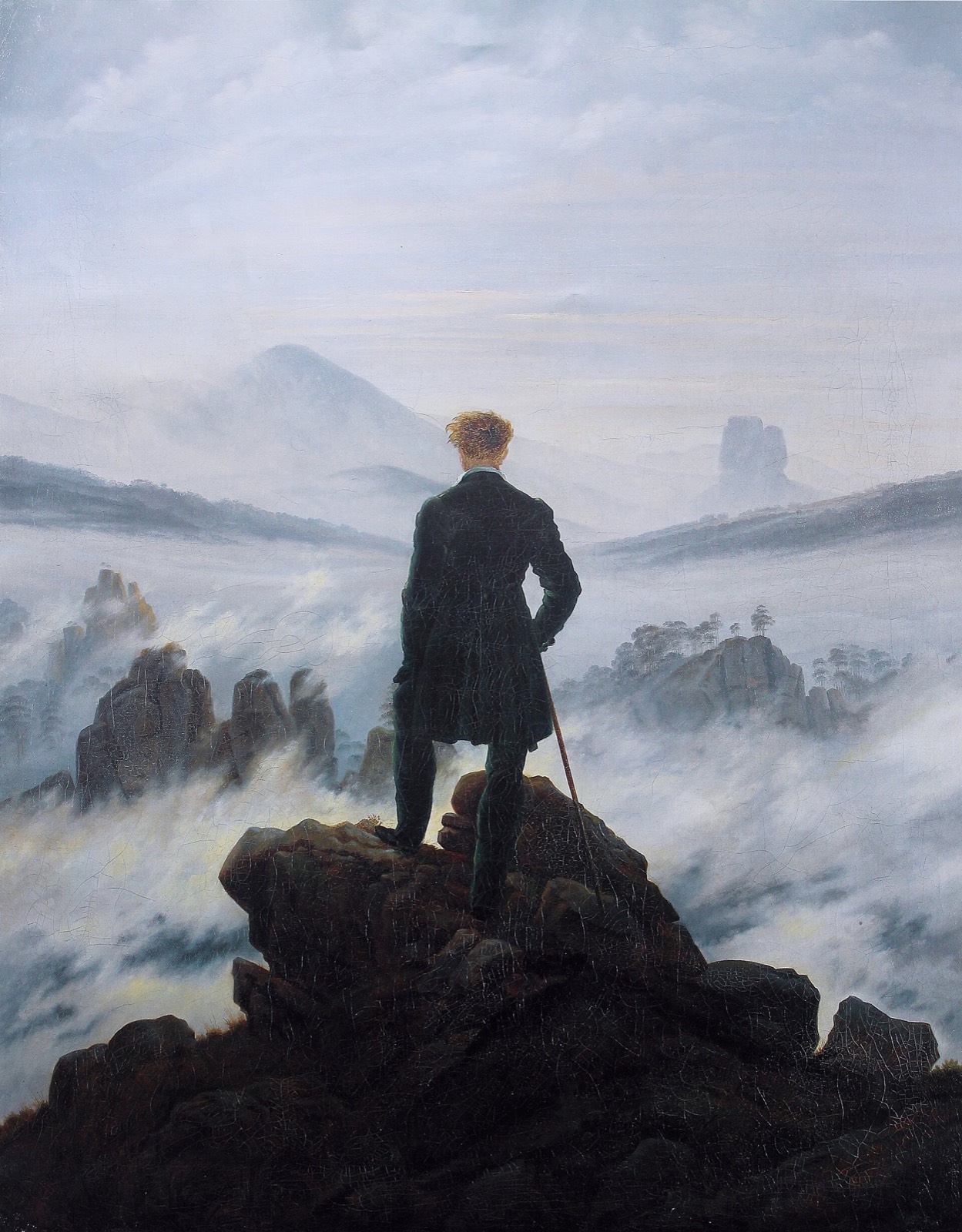 Un homme de dos sur un rocher contemple une mer de nuages